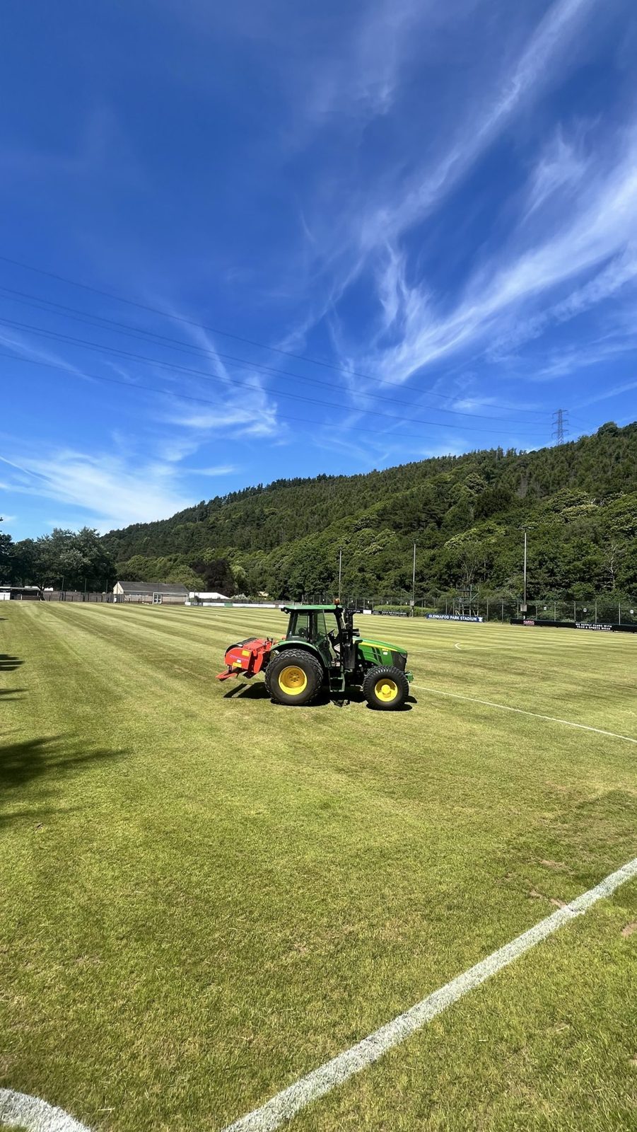 John Deere 5115M tractor on the football pitch at Goytre FC under a blue sky